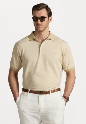 Beige polo shirt met een gestructureerd patroon, korte mouwen en een drieknoopsluiting. Gecombineerd met witte broek en een bruine riem.