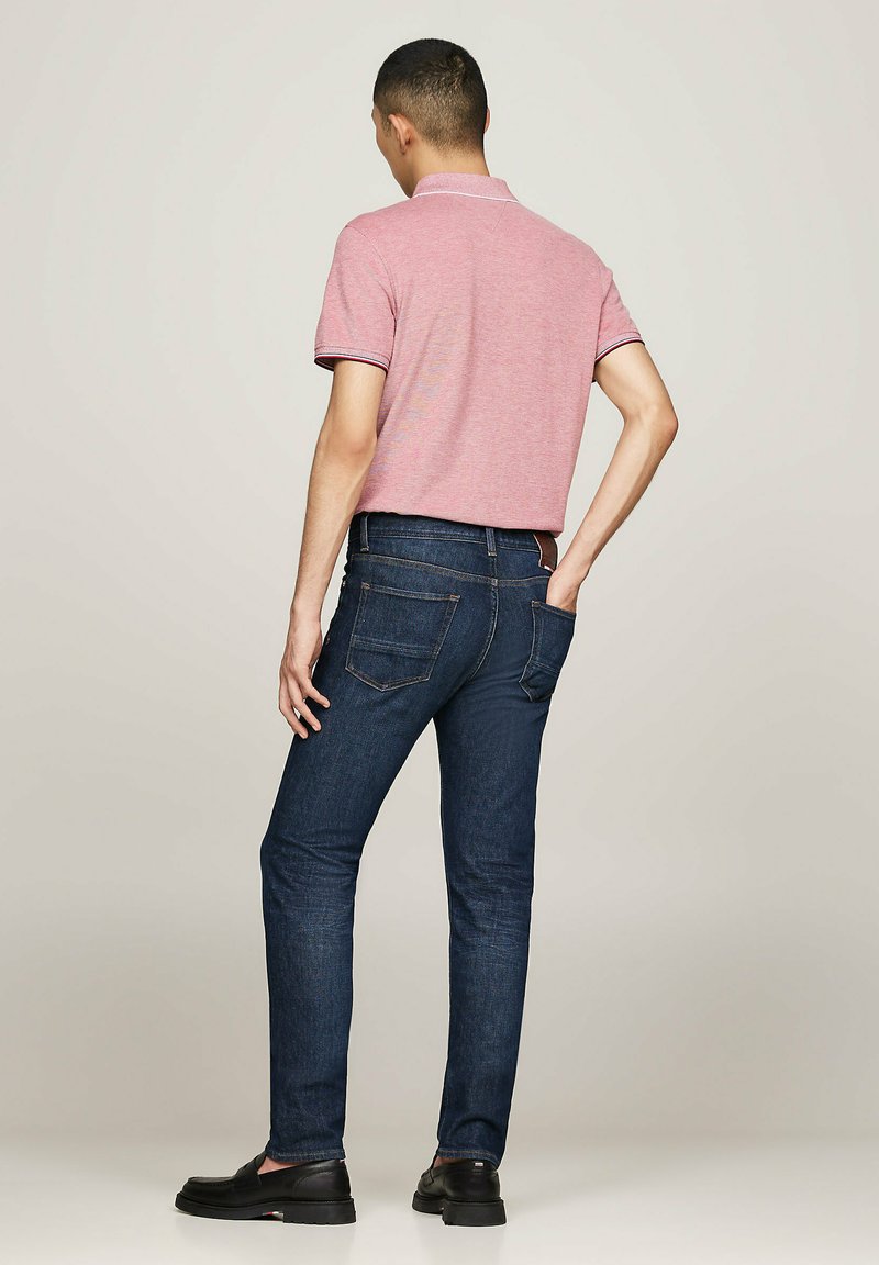 Herren-Fit-Polohemd in Hellpink mit Kragen, kombiniert mit dunkelblauen Denim-Jeans. Die Jeans haben ein klassisches Fünf-Taschen-Design und sichtbare Nähte.