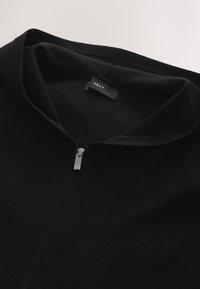 Hanorac negru cu fermoar, confecționat dintr-un material texturat, prevăzut cu un guler înalt și un fermoar argintiu. Etichetă cu logo-ul "NEXT" atașată în interior.