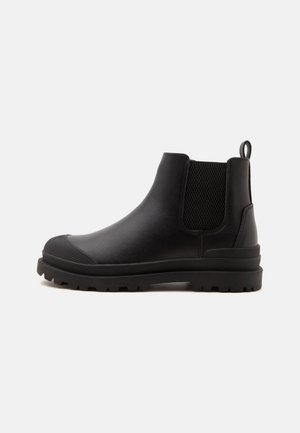 Bottine en cuir noir avec languette, panneau latéral élastique, embout en caoutchouc texturé et semelle épaisse à crampons.