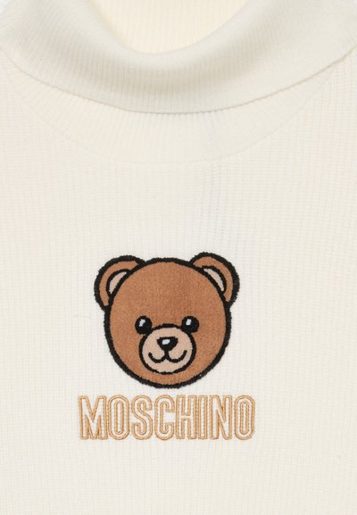 Krämfärgad ribbad muddkrage med brunt teddy-björn broderi och "Moschino" i gyllene tråd nedanför grafiken. Mjuk textur och figurnära design.