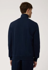Sudadera de tiro alto en azul marino con cuello alto, puños acanalados y dobladillo. Fabricada con un tejido suave, muestra costuras mínimas y un diseño limpio.