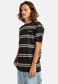 Camiseta a rayas negras con rayas horizontales crema, hecha de algodón. Presenta un cuello redondo y mangas cortas. Logo en el pecho.