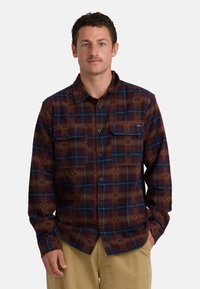 Geruite flanellen shirt in rood, bruin en blauw. Heeft twee borstzakken en een patroonontwerp. Lange mouwen met knopenmanchet.