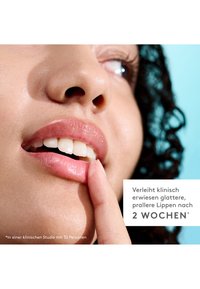 Lip product advertisement featuring glossy, pink lips with defined contours. A finger gently touches the lips. Background is light blue.