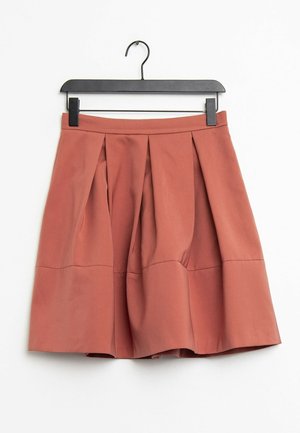 Une jupe plissée couleur rouille en tissu léger, avec une taille lisse et une forme évasée, accrochée à un crochet noir.