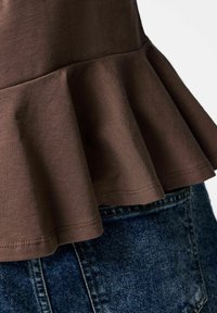 Brun bomullsbluse med peplumkant, som har en glatt tekstur og figursydd liv. Kombinert med denimshorts i blått stoff med lomme.