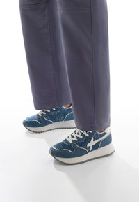 Sneaker sportive in denim blu con accenti bianchi, caratterizzati da ricami floreali, chiusura con lacci e una spessa suola bianca con fondo grigio testurizzato.