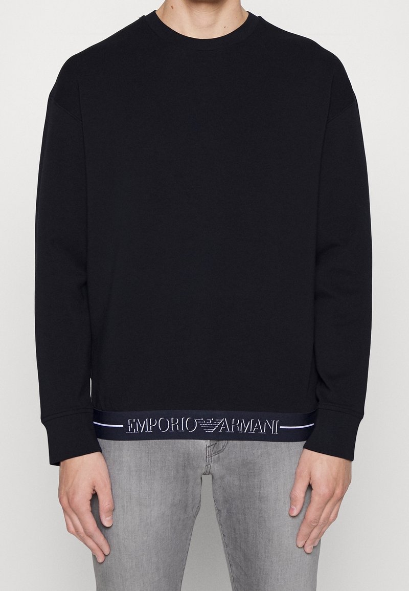 Svart sweatshirt med rund halsringning, långa ärmar och ett strukturerat logoband i marinblått vid fållen. Tillverkad i mjukt material.