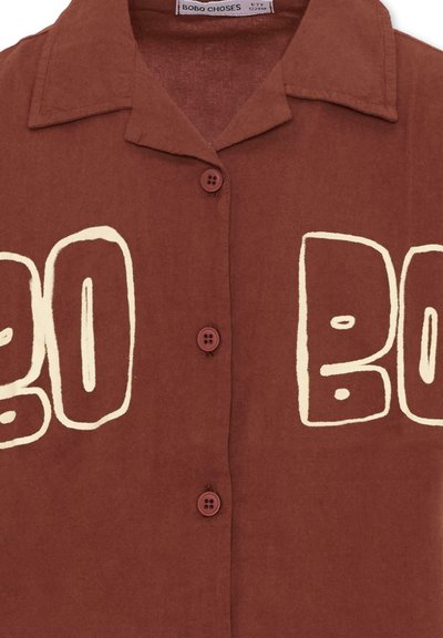 Camicia marrone con bottoni e colletto aperto, con grandi lettere bianche contornate "BOBO" stampate sul petto.