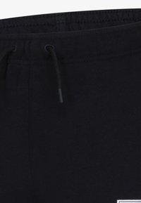 Svarta träningbyxor med elastiskt midjeband, snörning och en liten vit logotyp på låret. Mjukt material med en slät textur.
