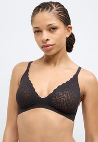 Μαύρο σουτιέν bralette με κυματιστό περίγραμμα, κατασκευασμένο από υφή υφάσματος με γεωμετρικό μοτίβο, υποστηριζόμενο από λεπτές ρυθμιζόμενες τιράντες.