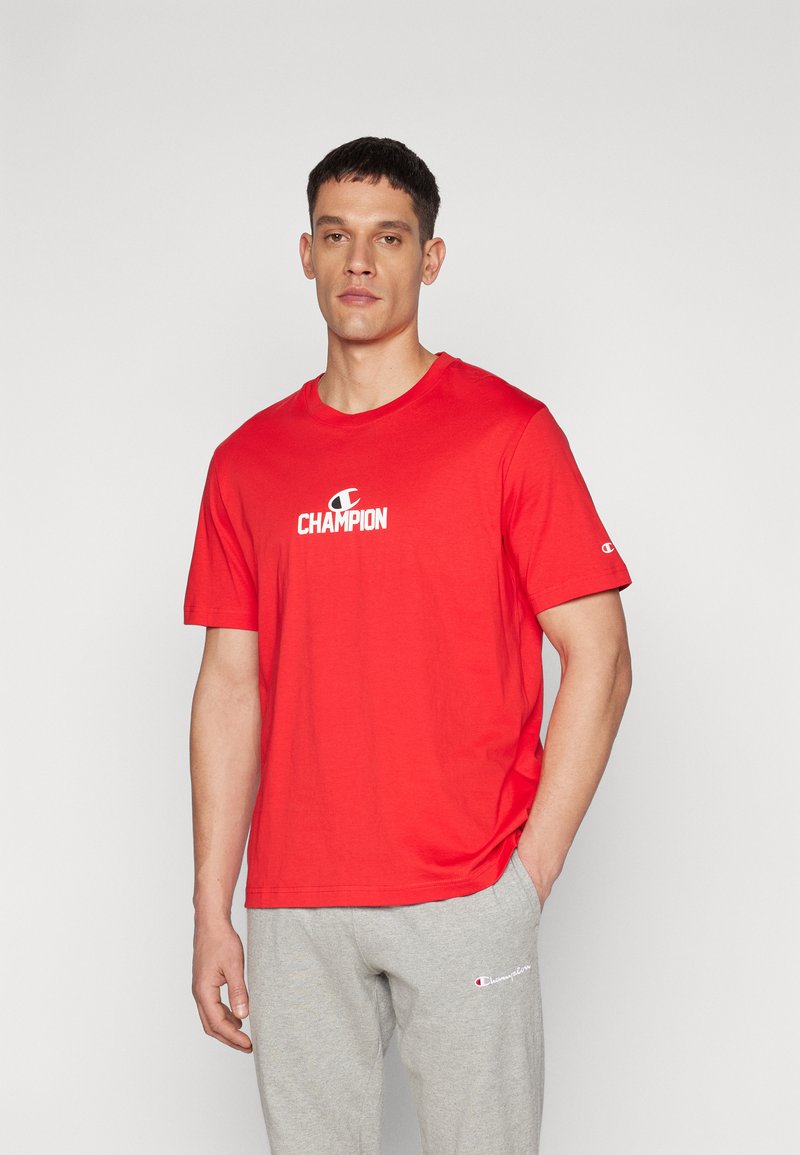 Rød bomulds t-shirt med et hvidt "Champion" logo på brystet. Korte ærmer, rund halsudskæring og en afslappet pasform.