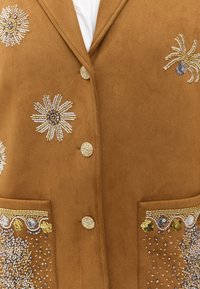 Gilet en daim marron avec broderie florale métallisée et accents en perles. Six boutons et poches à rabat avec des motifs décoratifs.