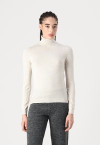 Pulover bej deschis cu guler înalt, într-un design ajustat, având un guler și manșete côtelate, asortat cu o pereche de pantaloni texturizați gri.