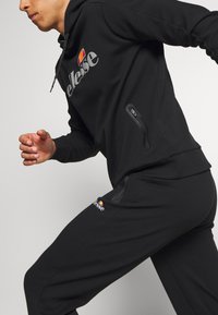 Black athletic tracksuit consisting of a hoodie with a logo and zippered pockets, paired with matching pants featuring similar logo detail.