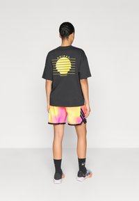 Μαύρο φαρδύ μπλουζάκι με κίτρινο γραφικό στην πλάτη, συνδυασμένο με πολύχρωμα σορτς σε αποχρώσεις gradient, μαύρες λεπτομέρειες και αθλητικές κάλτσες.