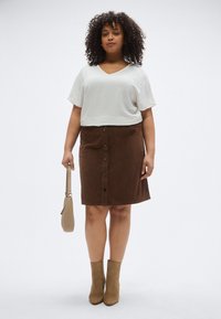 Λευκό τοπ με κοντά μανίκια και υφή ύφασμα, καφέ βελούδινη φούστα με κουμπιά μπροστά, μπεζ τσάντα και καφέ μποτάκια αστραγάλου.