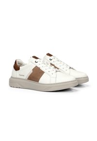 Zapatillas blancas con detalles en cuero marrón y malla, con cordones, cuello acolchado y suela de goma texturizada. Logo de la marca en el lateral.