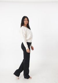 Maglione bianco lavorato a maglia con pois dorati, scollatura ampia, abbinato a jeans neri svasati e tacchi aperti trasparenti.