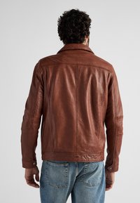 Brun läderjacka med krage, synliga sömdetaljer och en något sliten yta. I kombination med ljusblå denimjeans.