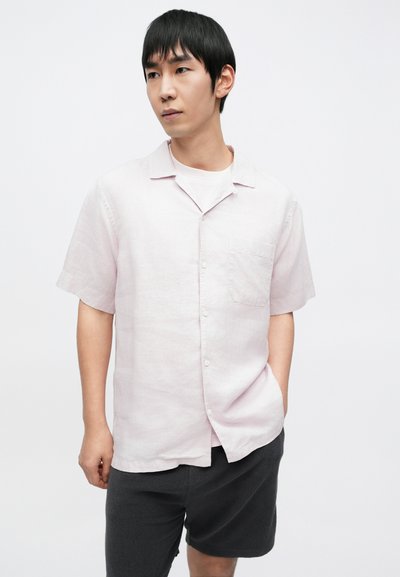 Chemise rose clair à manches courtes en lin avec une poche poitrine et un ourlet droit, associée à un short gris foncé, design minimaliste.