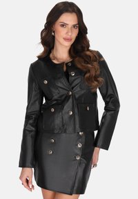 Giacca di pelle nera con dettagli dorati, caratterizzata da un design aderente, multiple tasche frontali e una lunghezza corta, abbinata a una gonna coordinata.