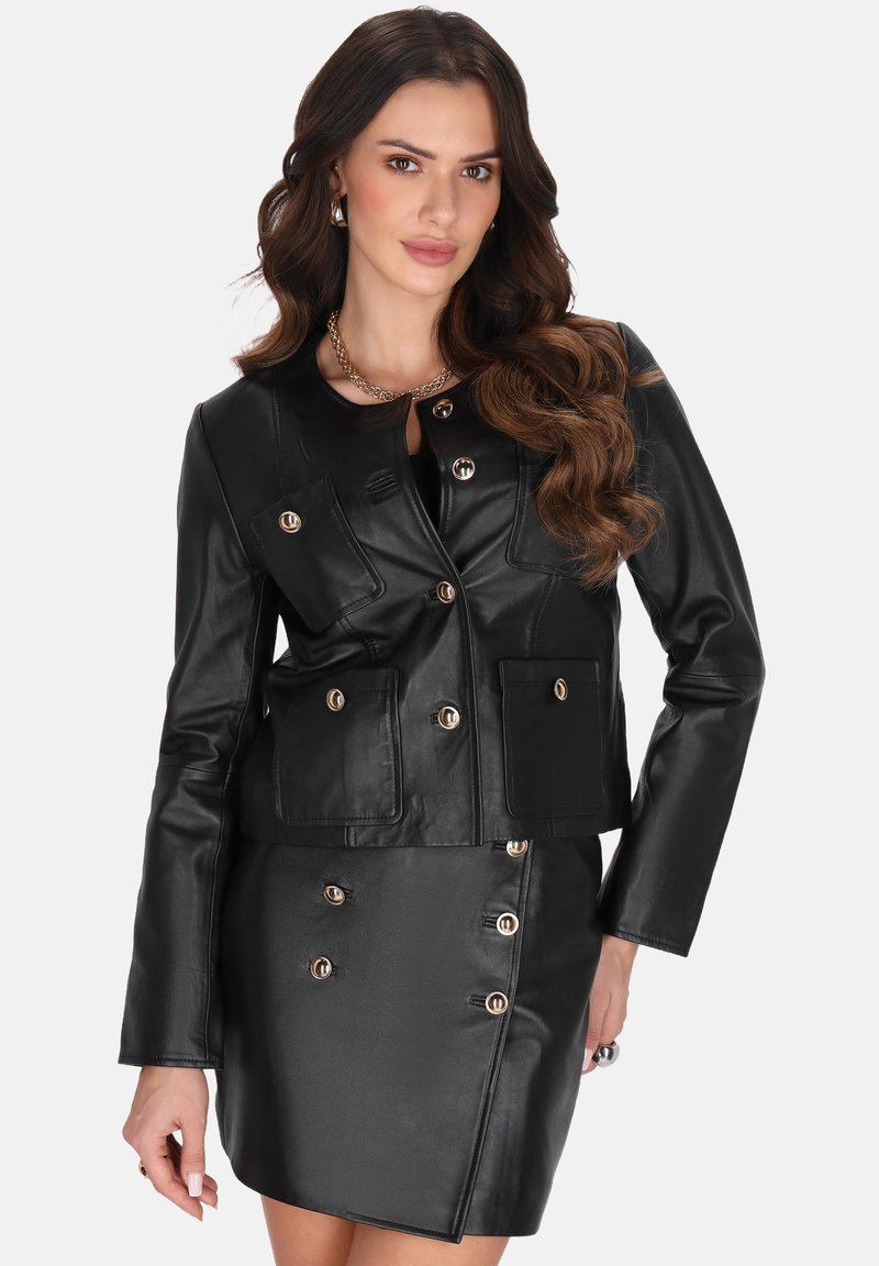Chaqueta de cuero negra con herrajes dorados, que presenta un diseño ajustado, múltiples bolsillos frontales y un largo corto, combinada con una falda a juego.