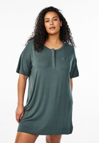 Īsām piedurknēm tērps tumši zaļā audumā, ar kabatu un plāksnes kakla dizainu, brīvā un neformālā piegriezumā.