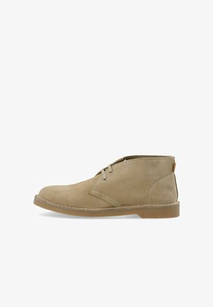 Beiger Wildleder-Wüstenstiefel mit zwei Ösen, genähter Sohle und niedrigem Knöchelkragen, seitlich auf weißem Hintergrund dargestellt.