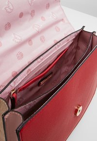 Czerwona i złota torebka o textured exterior. Wnętrze charakteryzuje się różowym wyścieleniem z wzorami. Wieloma przegrodami, w tym kieszonką na zamek.