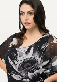 Zwart-wit top met bloemenpatroon, met een losse fit, doorschijnende mouwen, een ronde halslijn en decoratieve kralenaccenten op de stof.