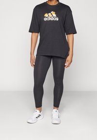 Black oversized t-shirt with a floral Adidas logo, paired with black leggings. White athletic shoes with black accents complete the outfit.