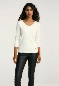 Biała bluzka z długim rękawem i dekoltem w serek, o prążkowanej teksturze i subtelnym logo. W połączeniu z czarnymi skórzanymi spodniami.