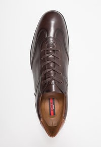 Chaussure en cuir marron à texture lisse, bout arrondi et design à lacets. La semelle intérieure présente le logo "LLOYD" en rouge et noir.