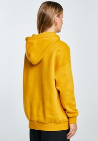 Żółta hoodie z miękkiego materiału, luźny krój i ściągacze. Posiada dużą kapturem oraz czysty, minimalistyczny design.