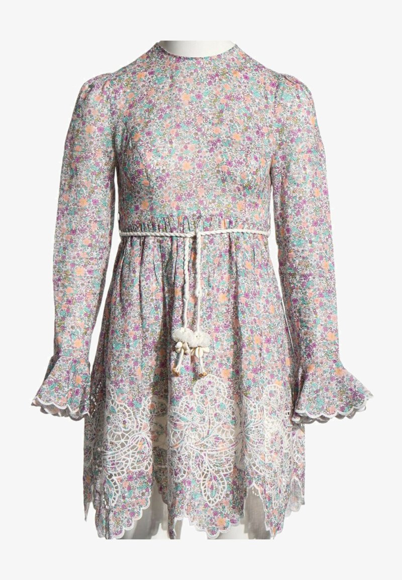 Robe fleurie à manches longues avec de petites fleurs roses, violettes et vertes, ourlet festonné en dentelle et ceinture blanche tressée avec des pompons à la taille.