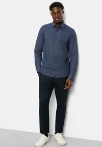 Langärmliges, marineblaues Hemd mit kleinem geometrischen Muster, durchgehende Knopfleiste, kombiniert mit dunklen Hosen und weißen Sneakers.