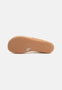 Reebok tenisica s potplatom od bež gume, koja ima teksturirani uzorak za bolje prianjanje i bijeli logo kao akcent, sa zaobljenim petom i ravnim profilom.