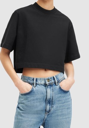 Persona que lleva una camiseta negra corta con cuello alto y unos vaqueros de tiro alto azul claro con las manos en los bolsillos.