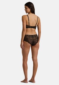 Sostén de encaje negro y pantalones cortos a juego, con intrincados patrones florales, bordes ondulados, tirantes ajustables y una apariencia delicada y texturizada.