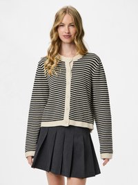 Femme aux longs cheveux blonds portant un cardigan à boutons rayé noir et blanc et une jupe plissée gris foncé.