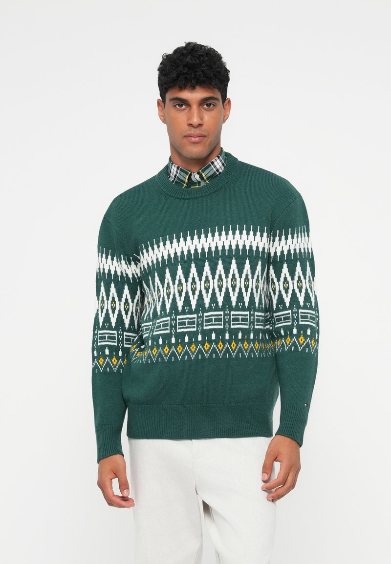 Green knitted sweater with a geometric white and yellow pattern. Ribbed neckline and cuffs, worn over a checkered collared shirt.