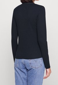 Czarny długi rękaw z prążkowanym wzorem, dopasowany krój, okrągły dekolt i gładka faktura, w połączeniu z jasnoniebieskimi jeansami z wysokim stanem.