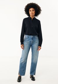 Černá košile s dlouhým rukávem na knoflíky spárovaná se světlými modrými jeansy s vysokým pasem a rozparky. Černé mokasíny dokončují vzhled.