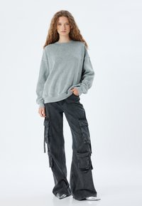 Felpa grigia con borchie decorative, abbinata a pantaloni cargo neri con molteplici tasche e una vestibilità a gamba larga. Calzature argentate.