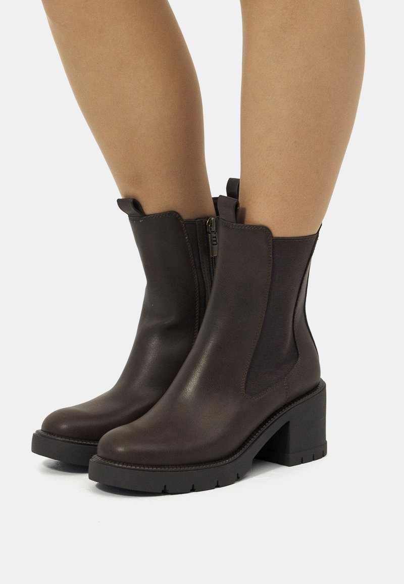 Bottes chevilles en cuir marron avec un talon bloque, fermeture éclair latérale et panneaux élastiques. Surface légèrement texturée et semelle en caoutchouc robuste.