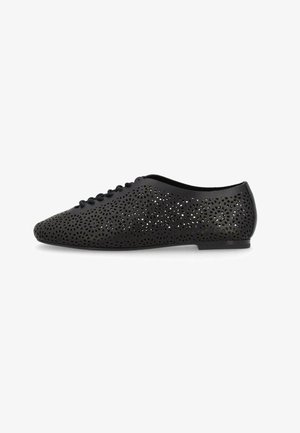 Scarpa piatta nera con motivi circolari traforati e allacciatura frontale, tacco basso e suola liscia, mostrata su sfondo bianco.