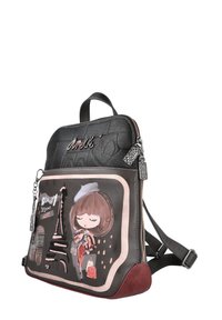 Mochila de cuero negra con una parte superior acolchada, que presenta una ilustración decorativa de una niña y la Torre Eiffel en un diseño enmarcado. Detalles en rojo.