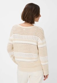 Maglione in beige lavorato a maglia con strisce aperte e testurizzate in modelli alternati. Presenta un ampio scollo e orlo e polsini a costine.